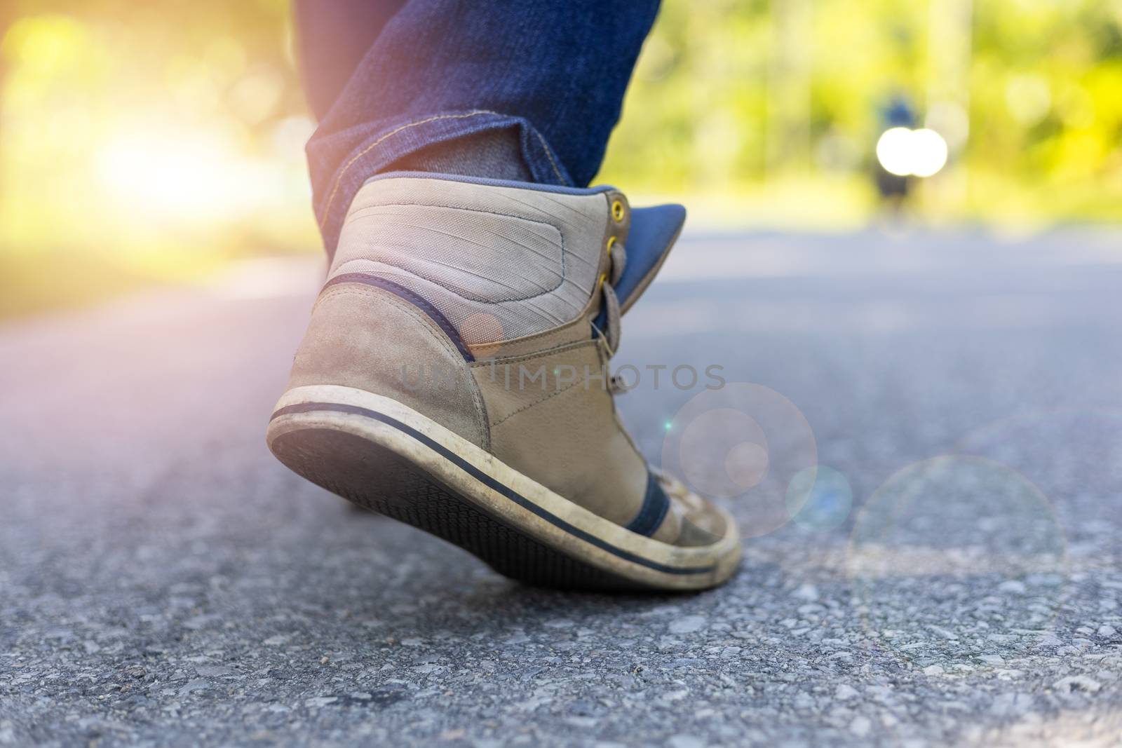 Man in jeans and sport sneakers walking on road. Focus on sneakers. Sun light effect. With copy space for text or desing