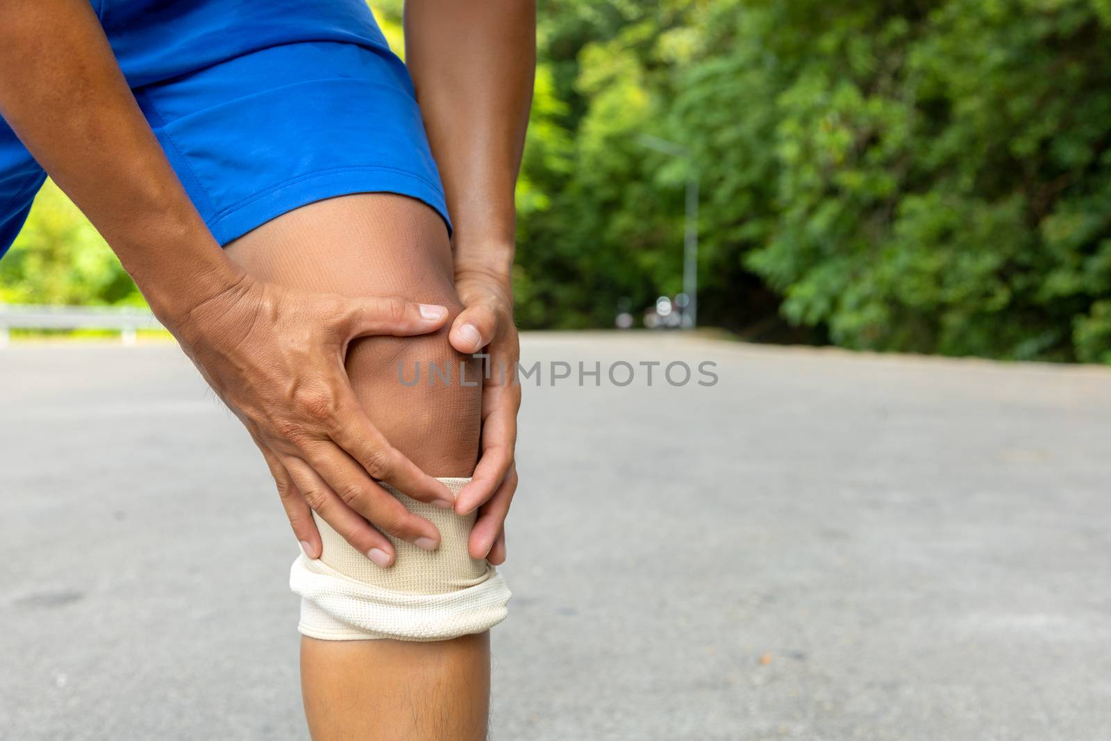Man with blue runing shorts use hands hold on his knee after running on road in morning time with copy space for text or design