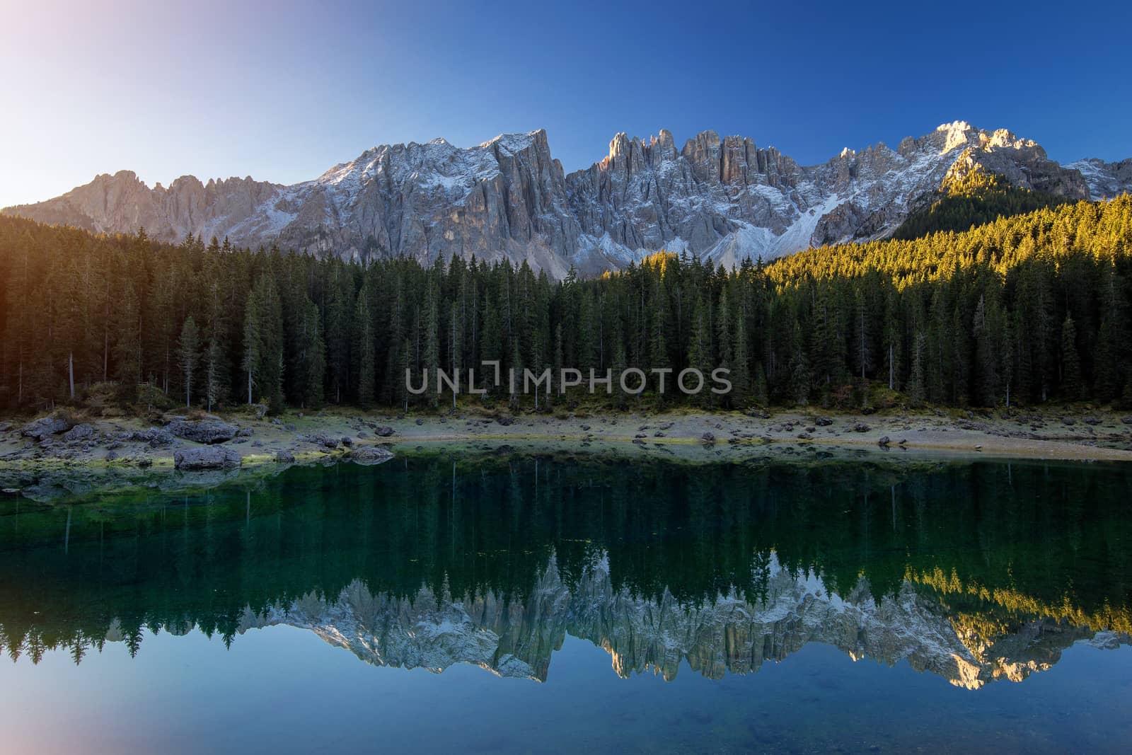 Beautiful sunrise at Carezza lake with light hitting the peaks, Dolomites, Italy