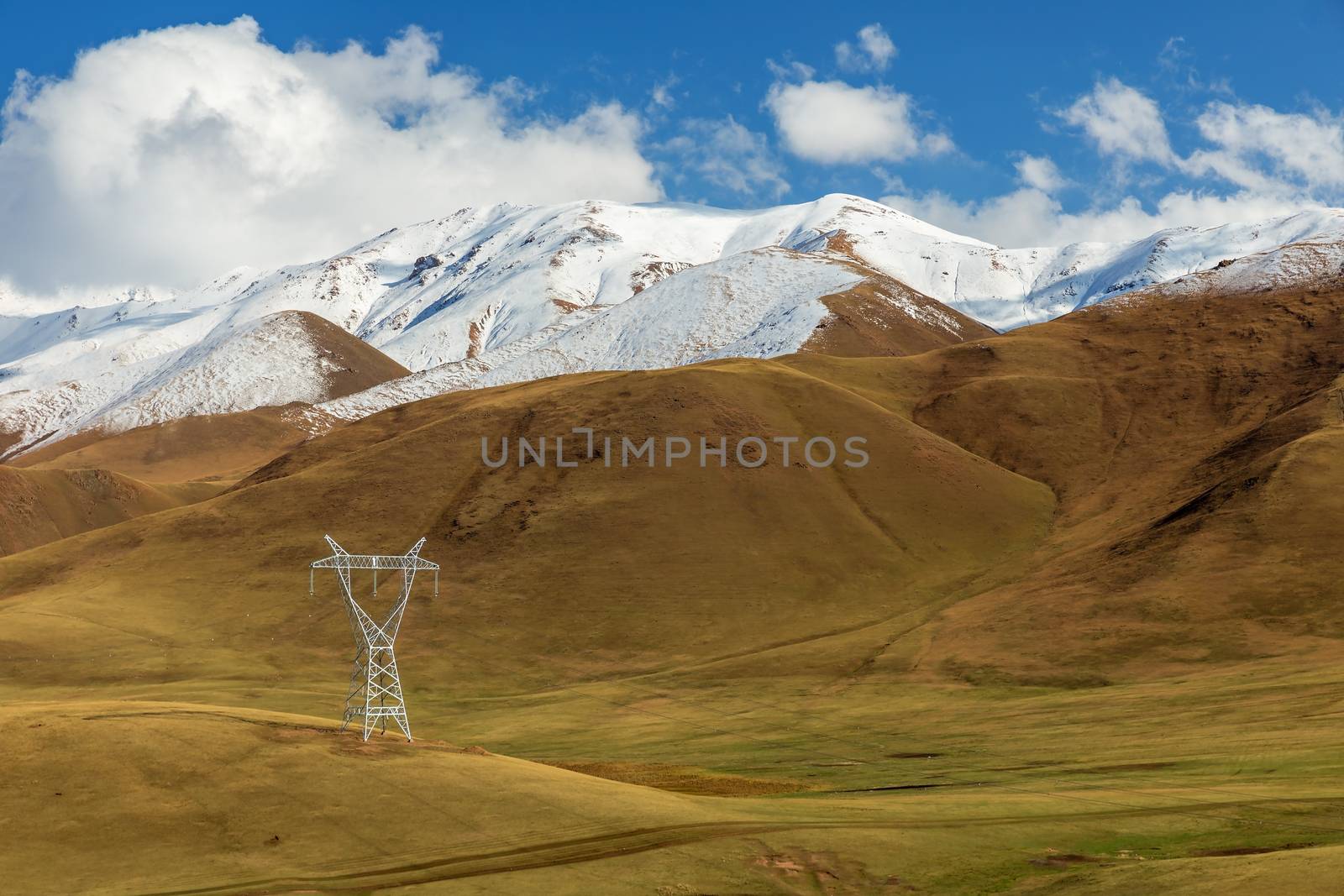 high voltage power line in the mountains of Kyrgyzstan, snowy mountains and green meadows