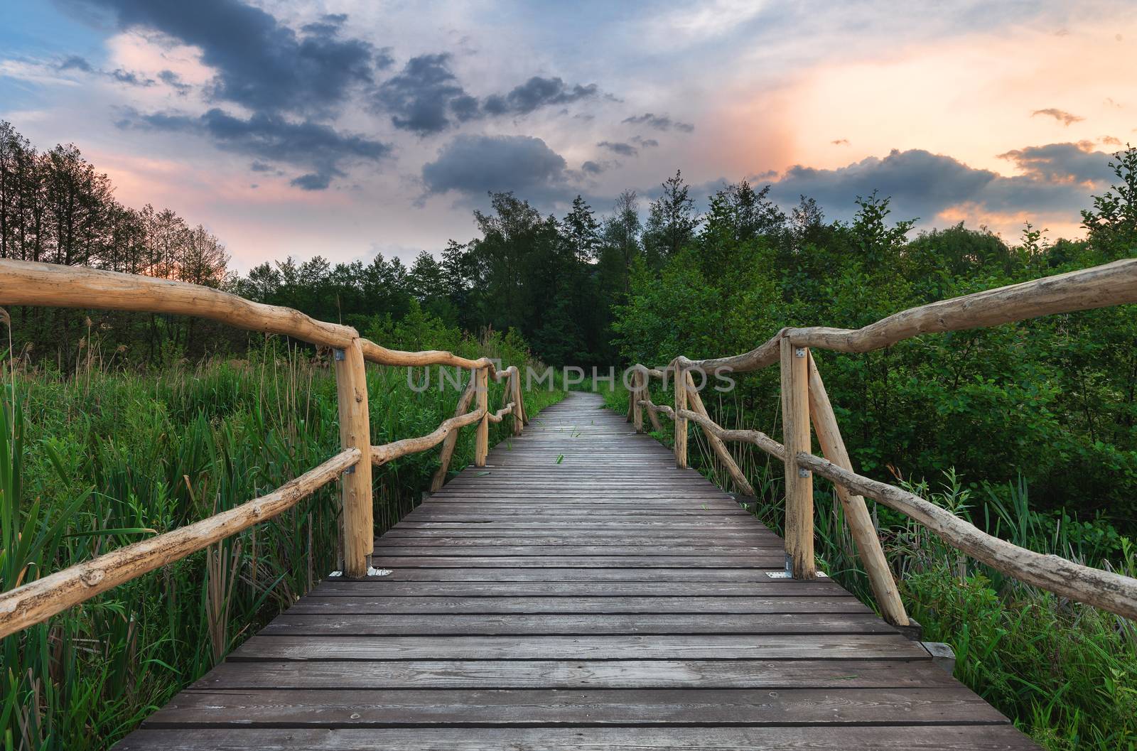 Wooden path bridge over lake at sunset after the storm by necro79