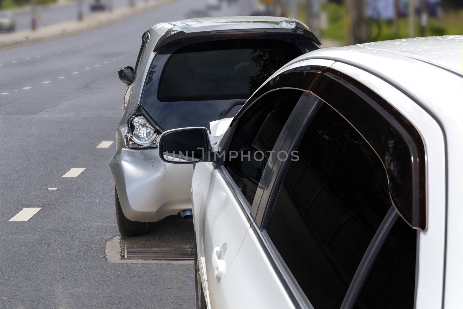 Front of white color car crash with back side of black color car damaged and broken by accident on city road.