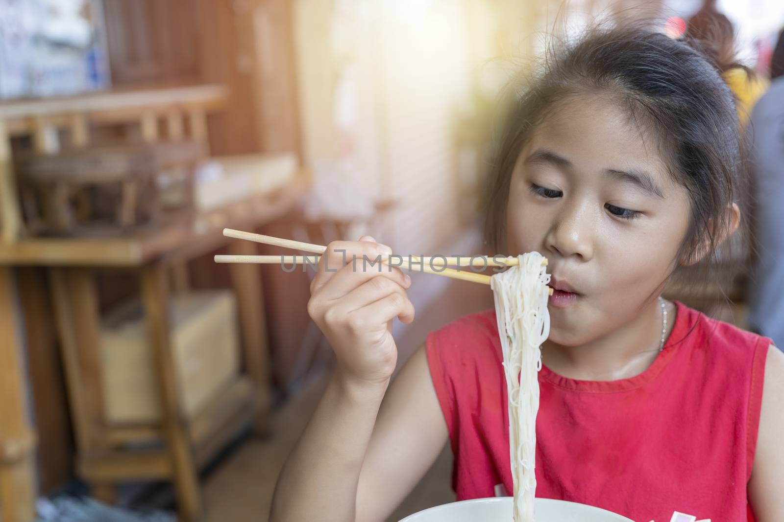 Asian child girl with red dress eating small noodles soup with chopsticks