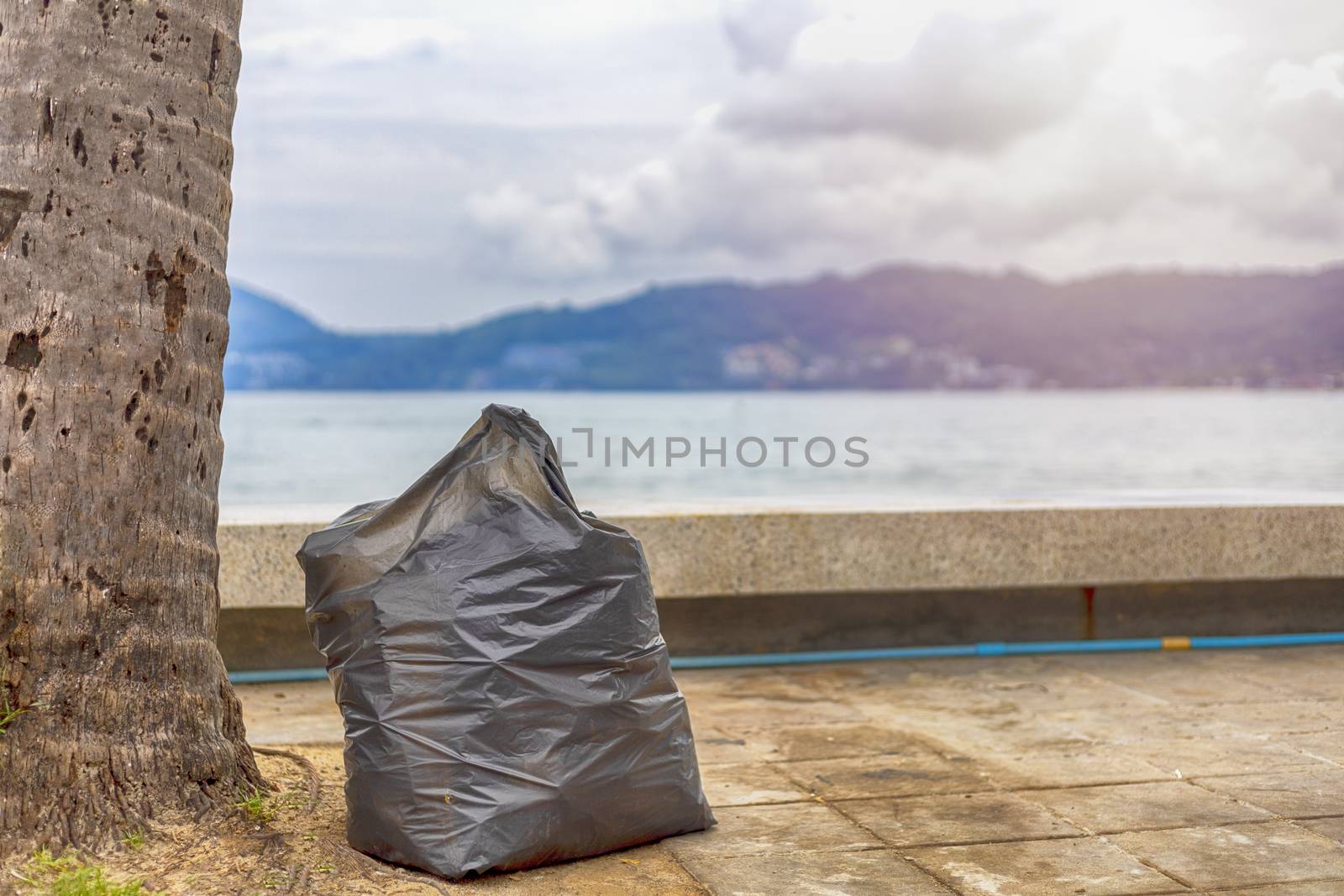 environment concept. Big plastic garbage bag on sidewalk under coconut palm tree near the beach.