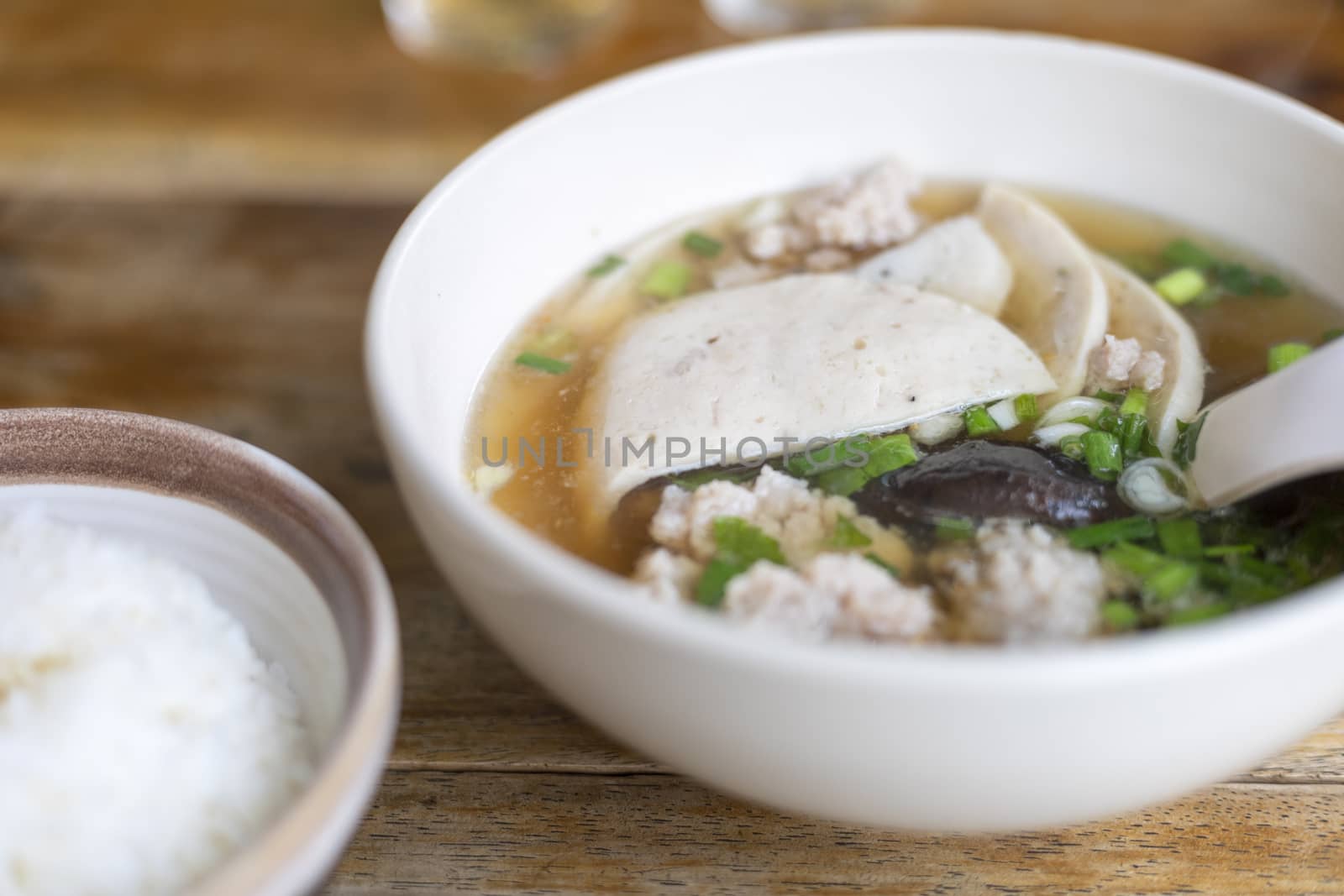 Soup with pock, pock stick, mushroom, vegetable in white bowl near have rice in small bowl on wood table. with copy space for text or design