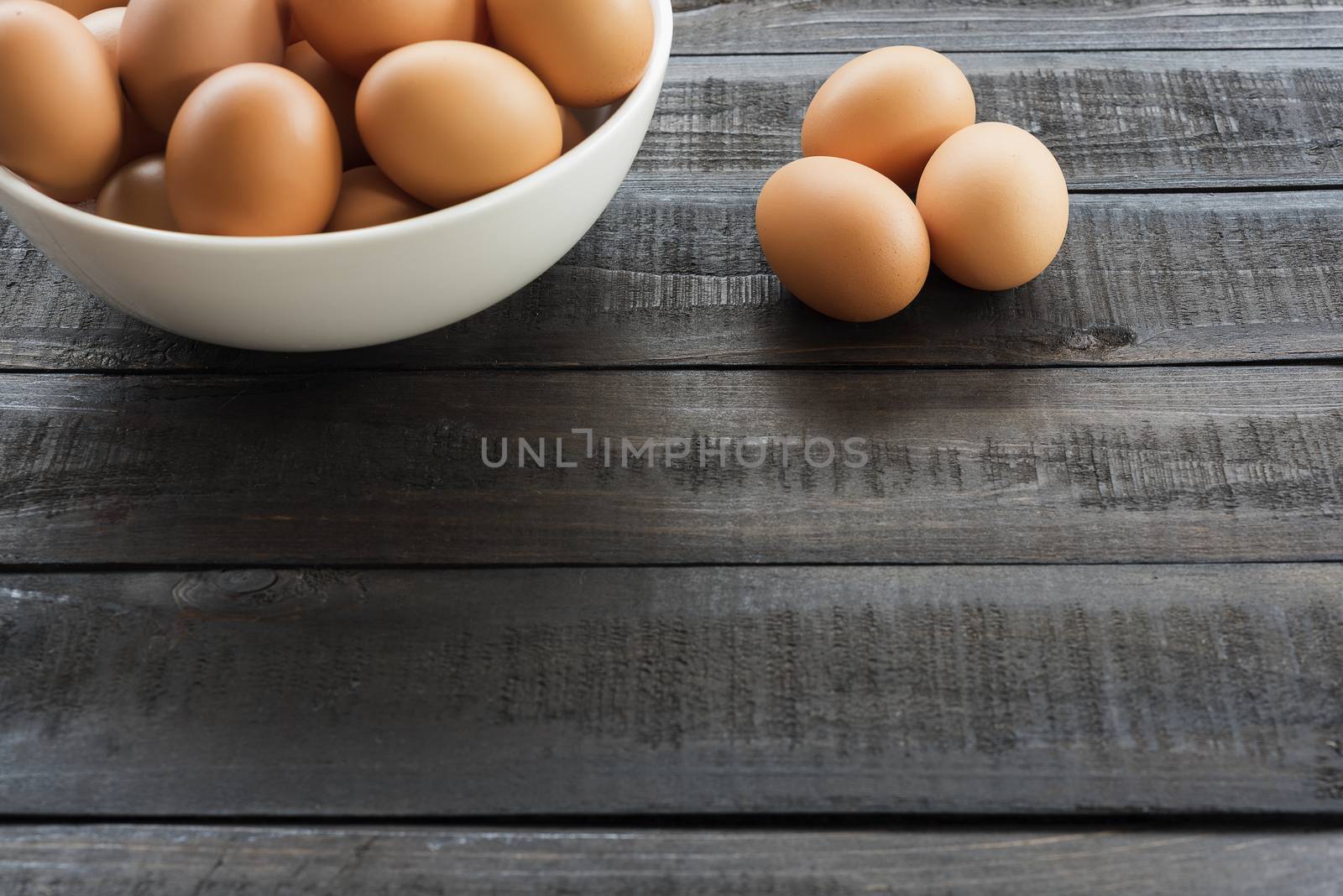 Chicken egg in white bowl and 3 chicken egg out side on Black color wood table