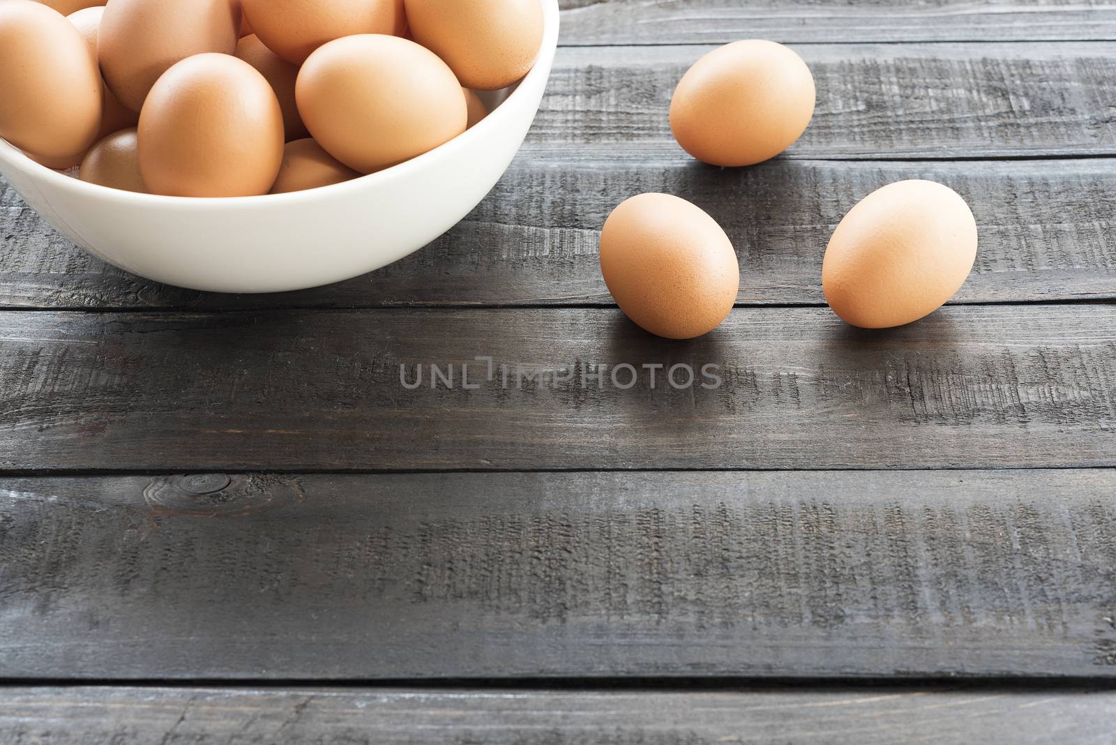 Chicken egg in white bowl and 3 chicken egg out side on wood table