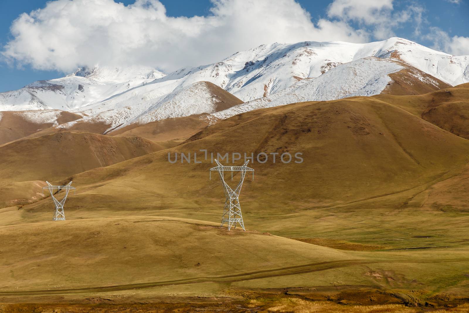 pylons of high-voltage power lines in the mountains, snowy mountain peaks and blue sky