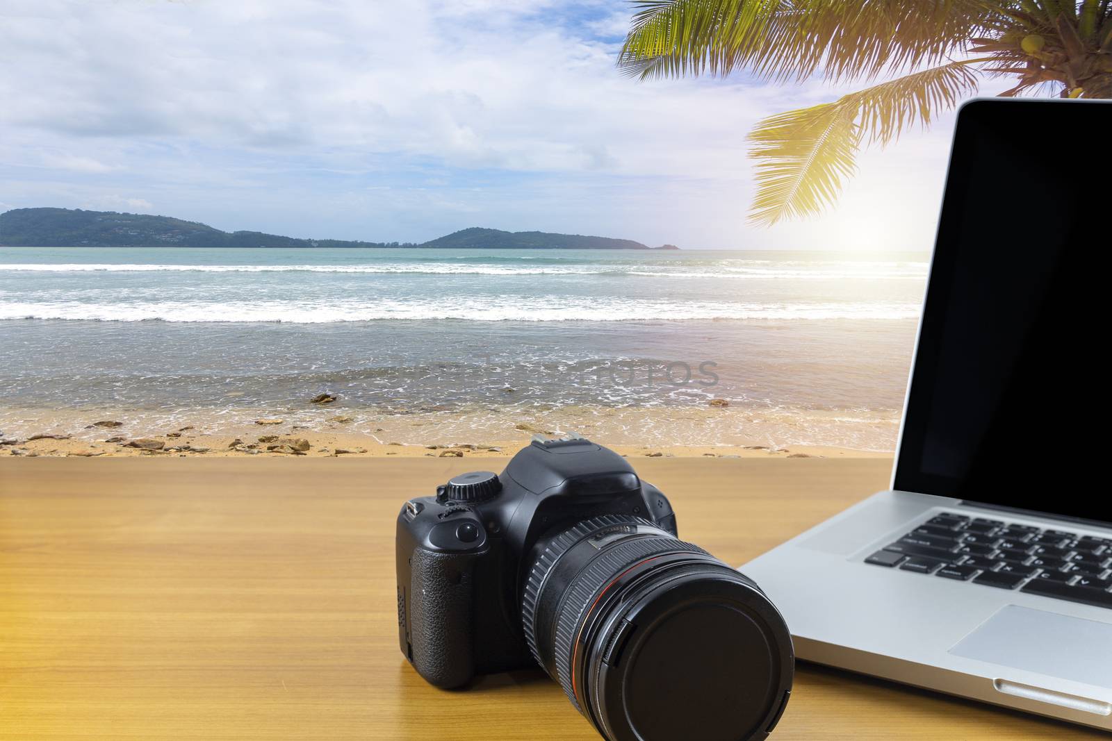 Digital camera and laptop on wood table with sea and sky background. With copy space for text or design.