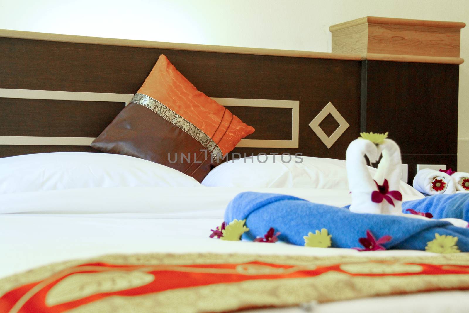 Two swans made from white towels are kissing on bed with yellow flower and orchid. White pillow and wood bed head.