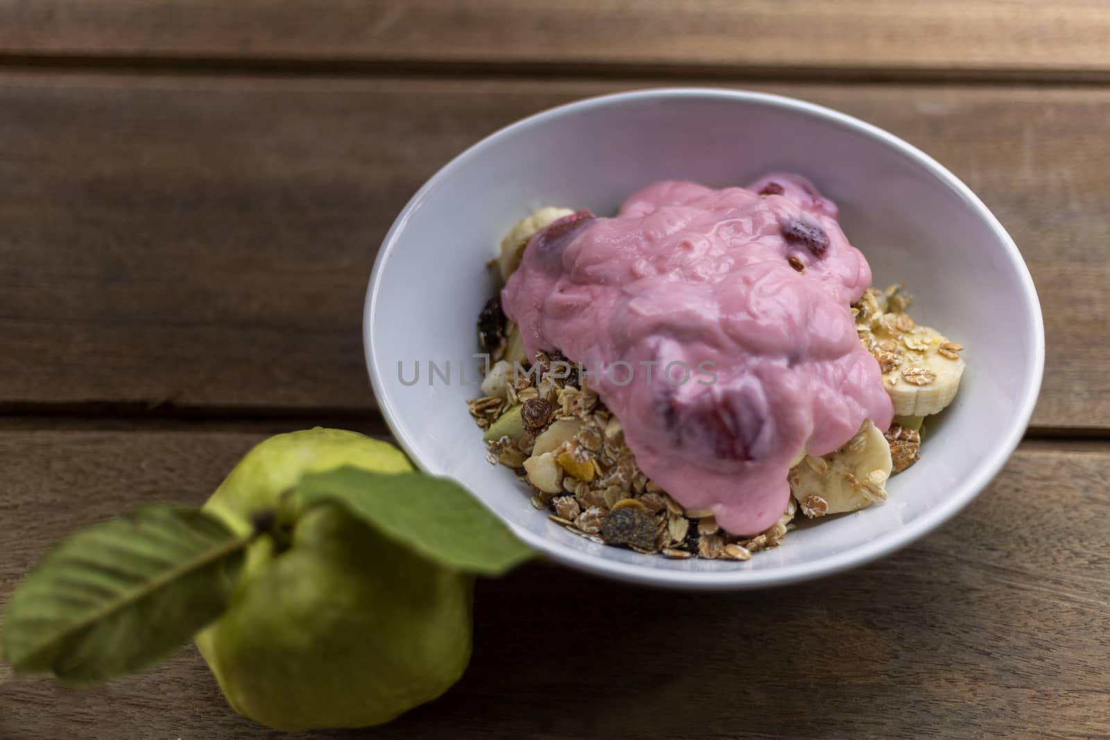 Healthy food yogurt strawberry, banana, guava, and oat in white bowl on wood table.