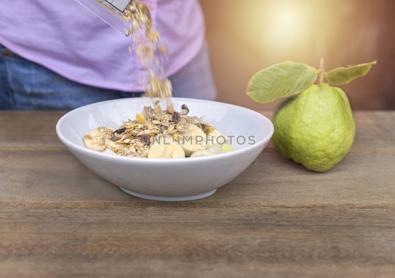 Women pour oat flakes from plastic bag to bowl and in bowl have banana slide , guava on wood table