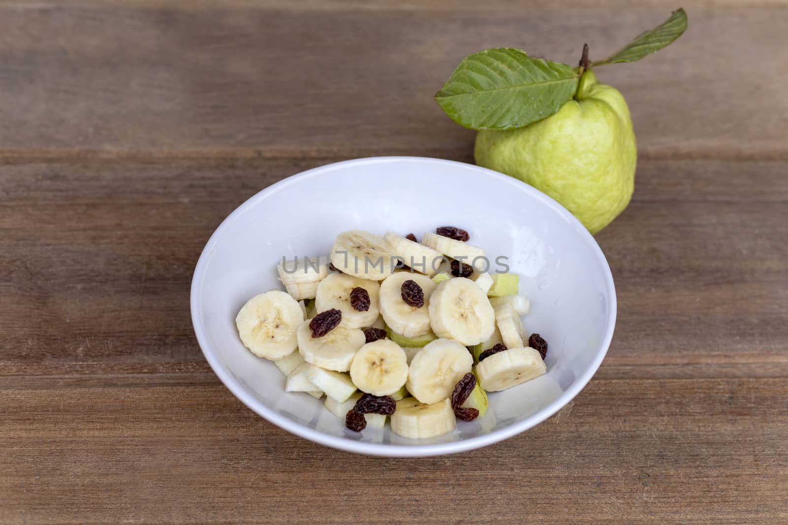 healthy food banana slide guava block and raisins in white bowl on wood table. With copy space for text or design.