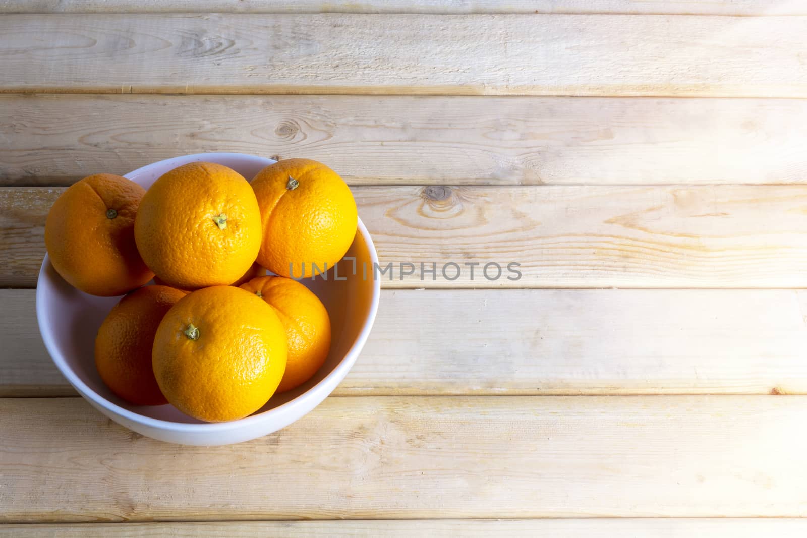 Fresh oranges in white bowl on wood table. With copy space for text or design.