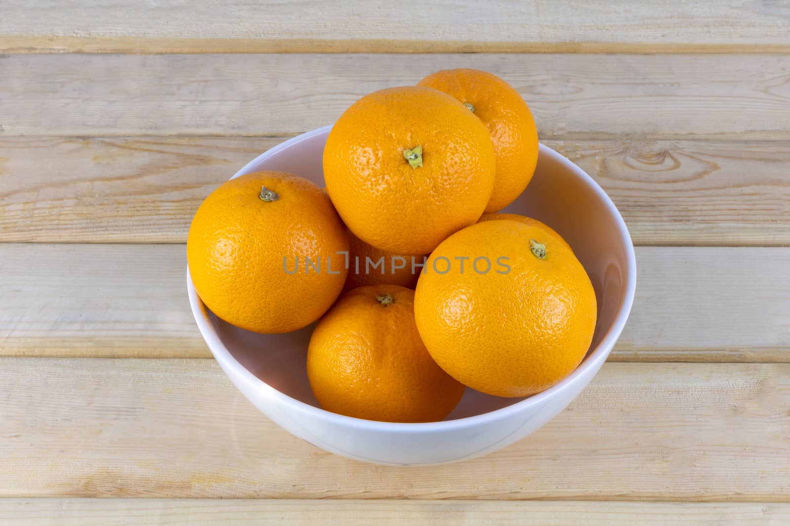 Fresh oranges in white bowl on wood table.