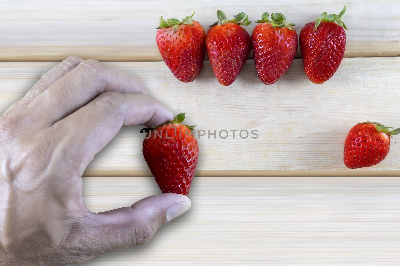 Hand man holding fresh strawberrie with fresh strawberries on wood table background with copy space for text or design.