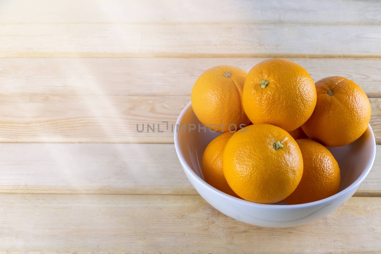 Fresh oranges in white bowl on wood table.