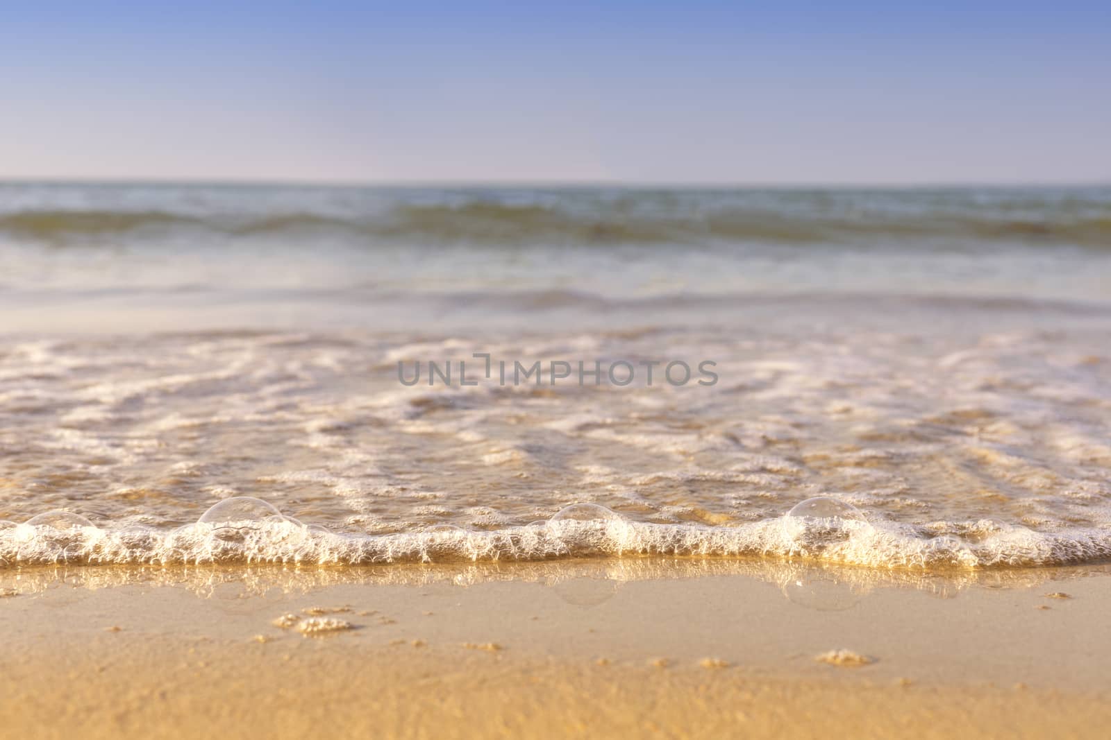 Soft wave from sea come to wet sand beach with blur clear sky background. With copy space for text or design