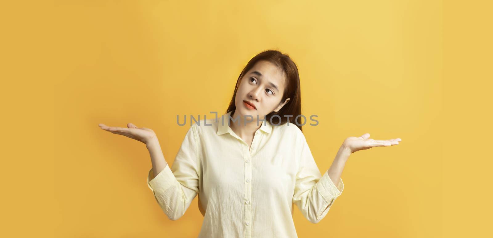 Beautiful Asian women showing open two hand palm and looking sideway on yellow background with copy space.