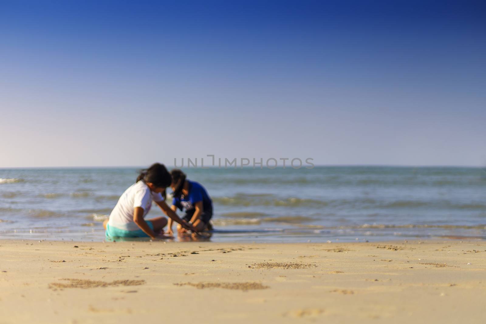 Holiday concept. 2 gril play sand on the beach with clear sky ba by Satrinekarn