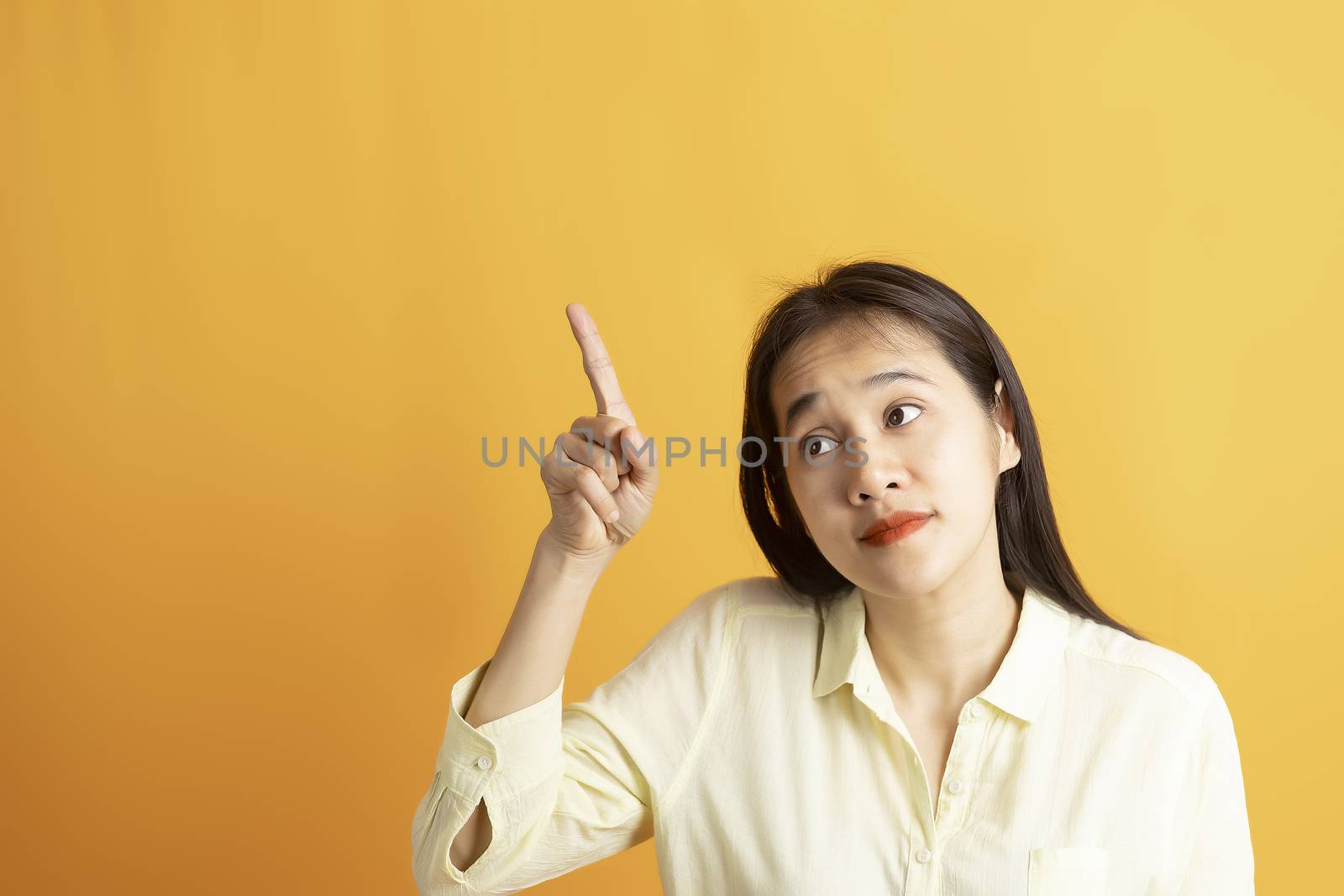 Beautiful smiling Asian woman show pointing  hand to empty space aside studio shot on yellow background with copy space. Asian women with hand pointing isolated on yellow backdrop.