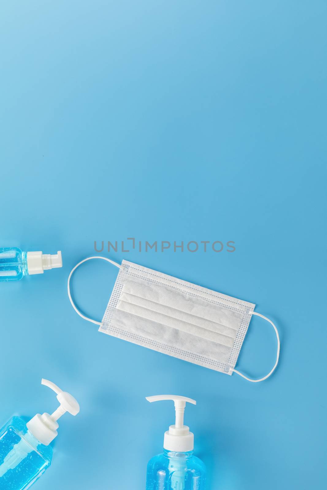 Top view medical face mask and  3 Different  bottle alcohol gel on light blue background with copy space. Face mask and hand sanitizer gel in pump head bottle.