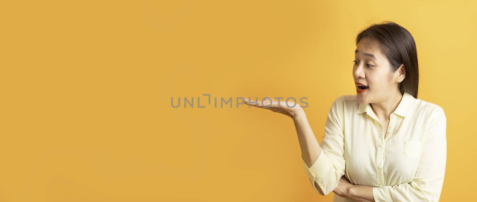 Beautiful Asian women showing open hand palm and looking sideway on yellow background with copy space.