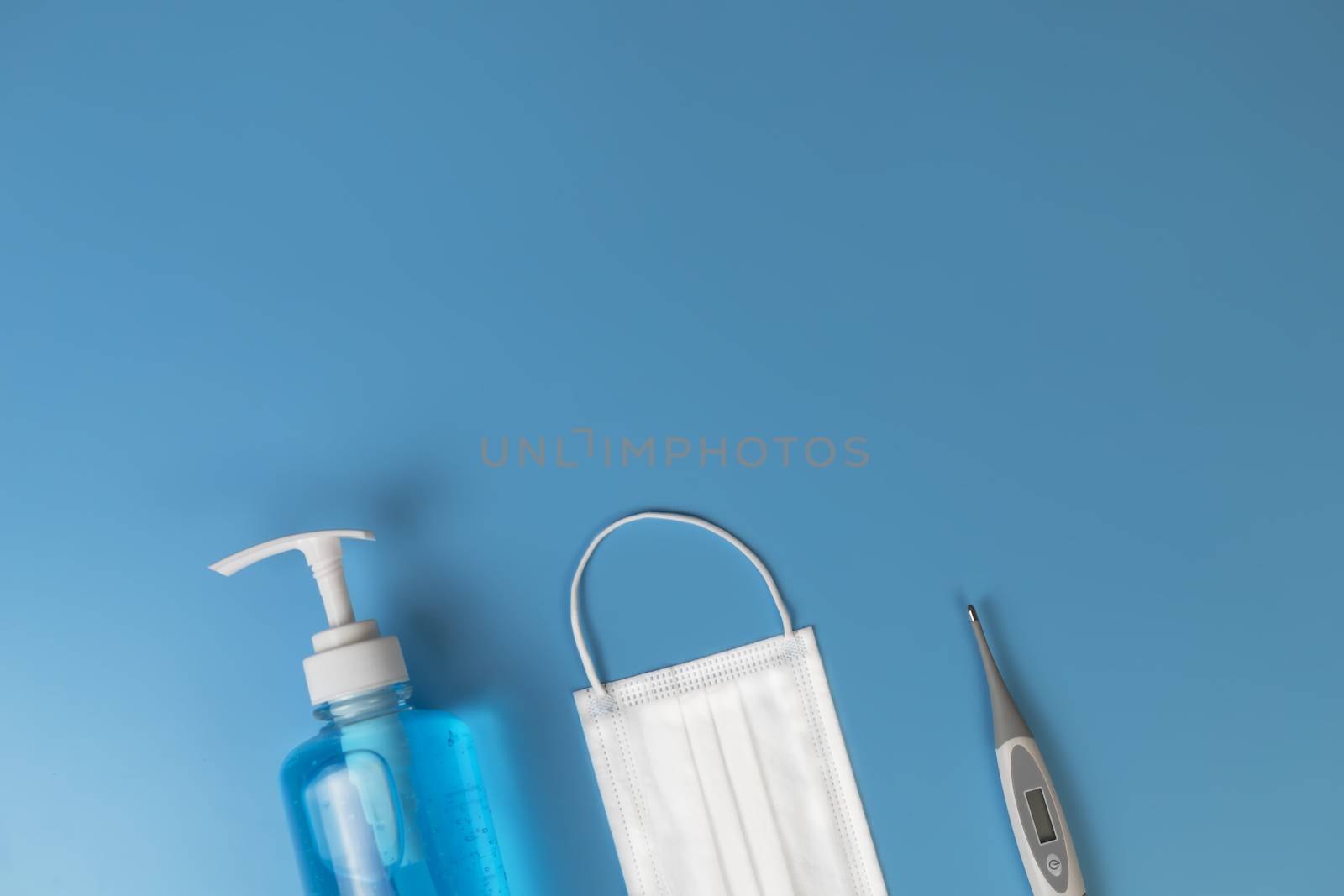 Hygienic masks digital thermometer , alcohol spray on blue baxkground. Medical face mask, alcohol sanitizer, thermometer on blue background with copy space.