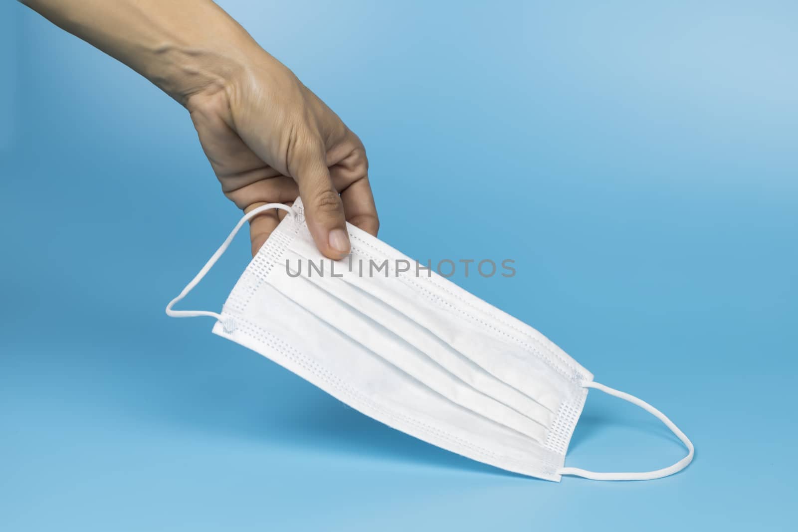 Women hand pickup and hold medical face mask on blue background. Women hand hold medical protective mask on blue background with copy space.