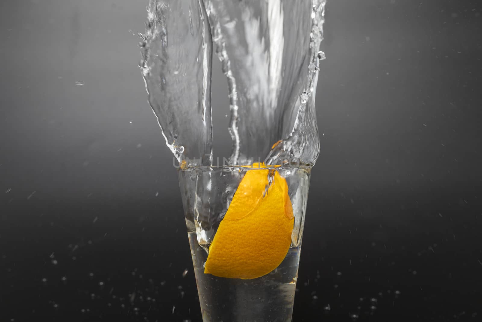 Orange slice falling and dropping into a splashing glass with black background.