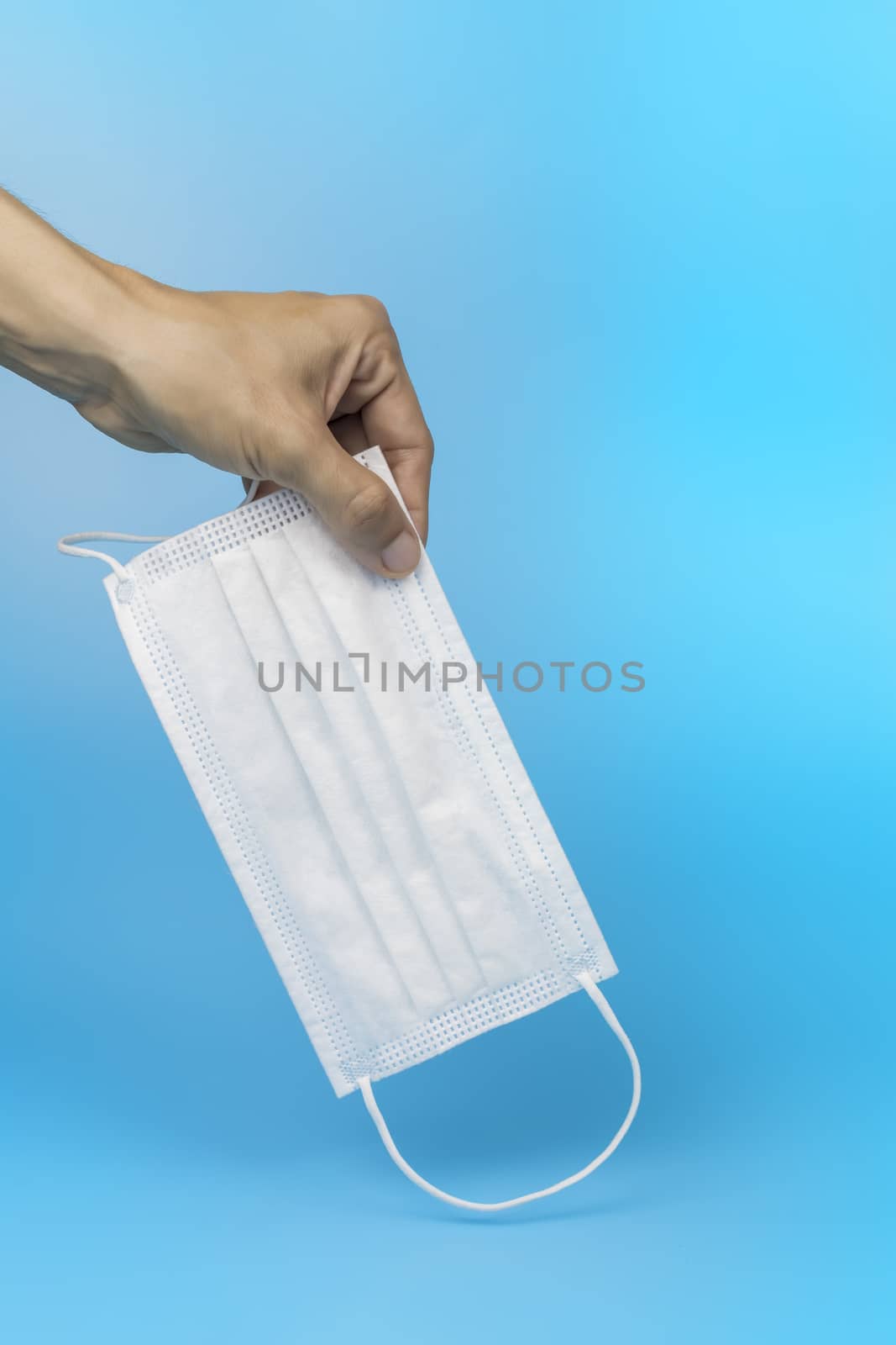 Women hand pickup and hold medical face mask on blue background. Women hand hold medical protective mask on blue background with copy space.
