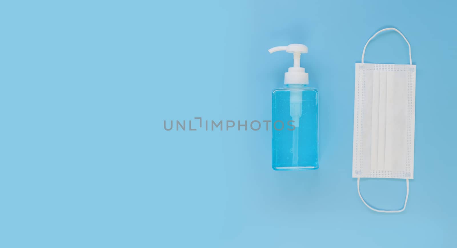 Top view medical face mask and alcohol gel on light blue background with copy space. Face mask and hand sanitizer gel in pump head bottle.