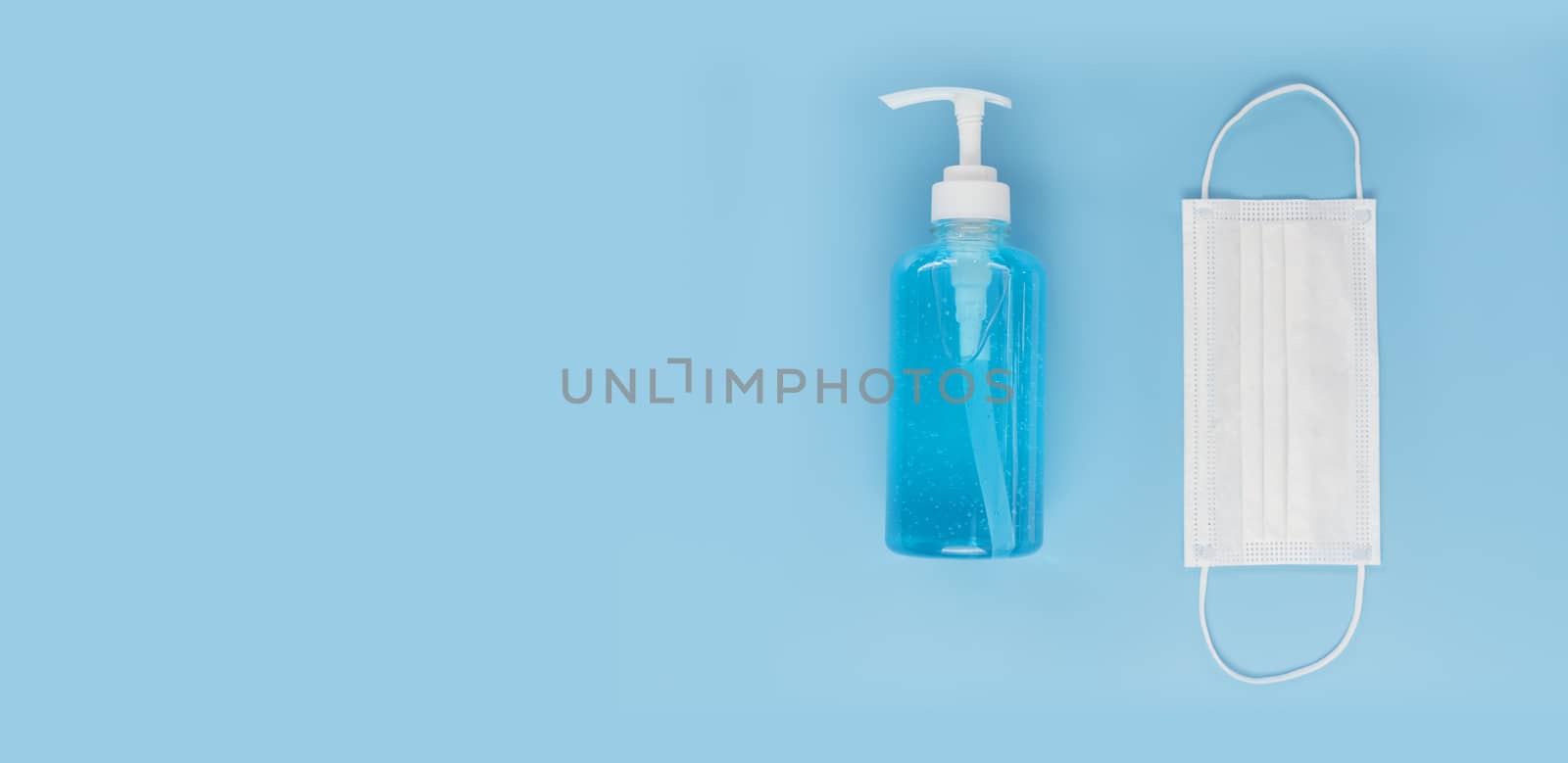 Top view medical face mask and alcohol gel on light blue background with copy space. Face mask and hand sanitizer gel in pump head bottle.