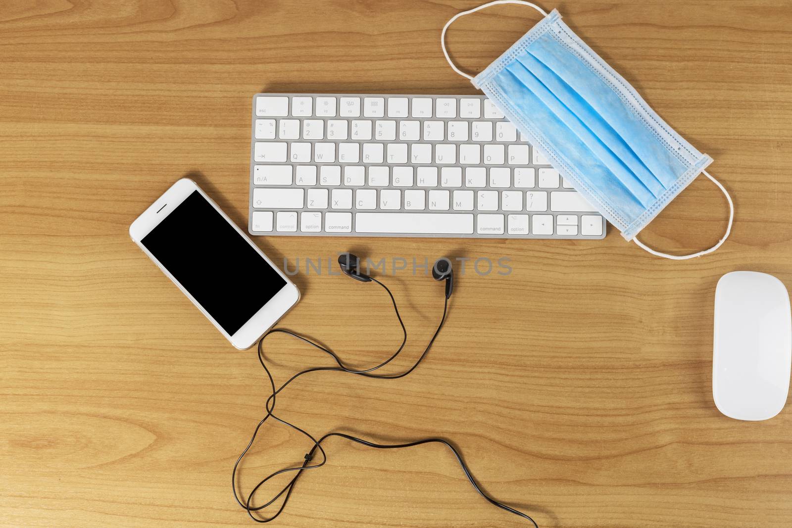 Top view keyboard, mouse, smartphone, headphone and face mask on wood table with copy space for text or design.