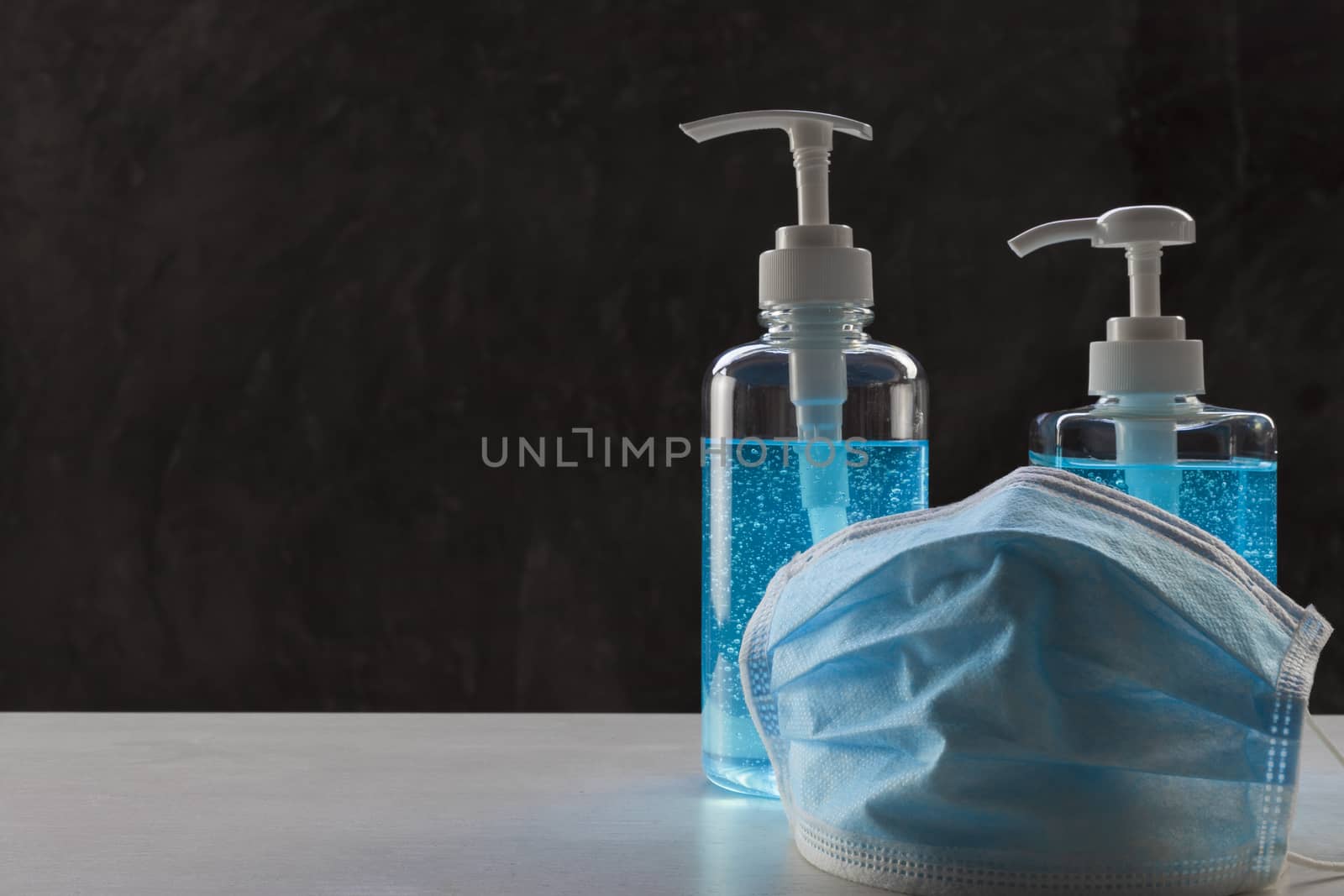 Face mask with alcohol sanitizer gel hand wash on wood table and raw cement background with copyspace for text or design.