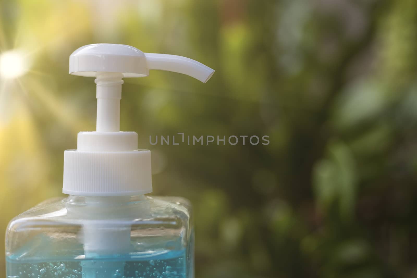 Close up pump of Blue alcohols gel bottle on blur green nature background and sun ray.Hand sanitizer gel in pump bottle. With copy space for text or design.