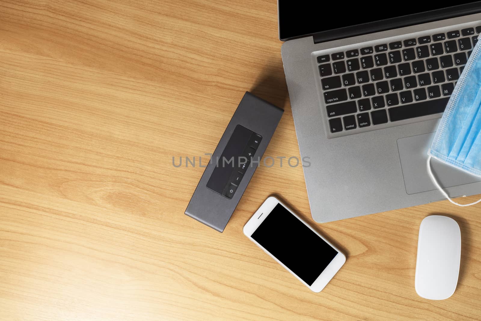 Work from home concept. Top view laptop, mouse, smartphone, speaker and face mask on wood table with copyspace for text or design.