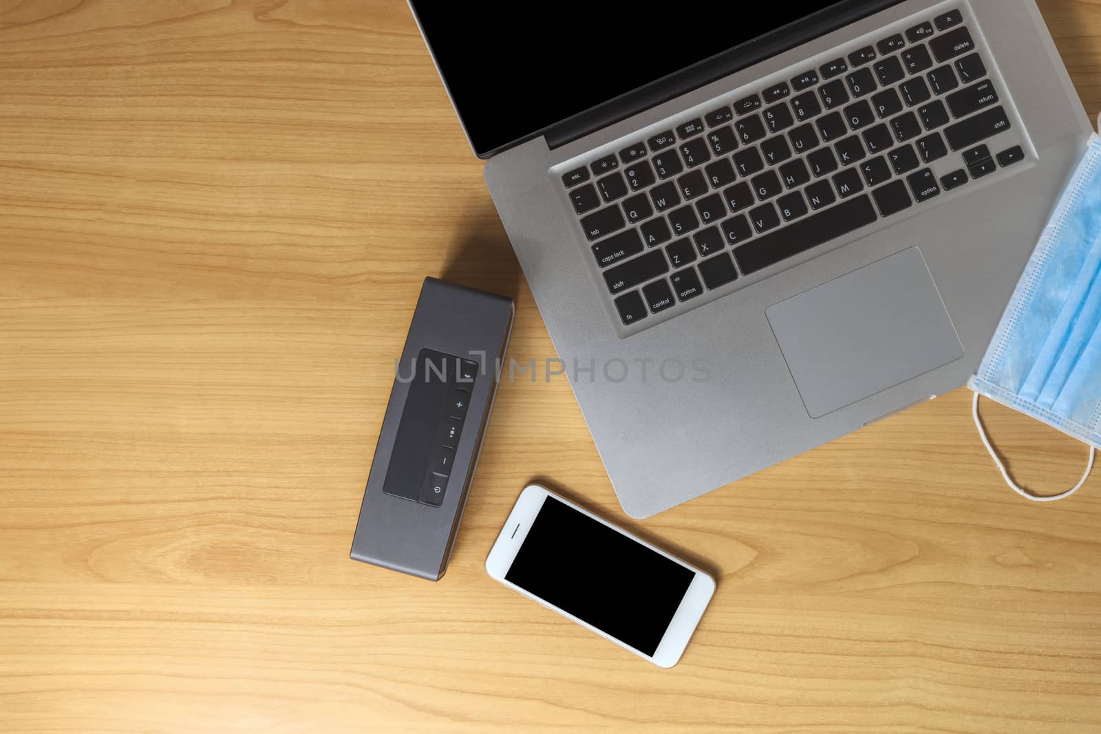 Work from home concept. Top view laptop, smartphone, speaker and face mask on wood table with copyspace for text or design.