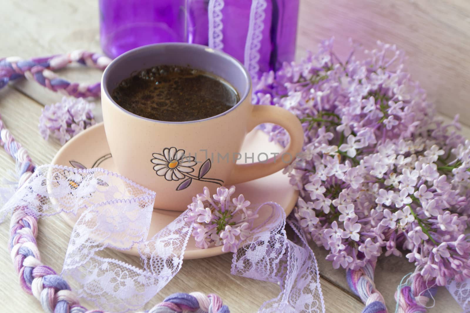 Violet cup of morning coffee or cappuccino and delicate purple, lilac flowers. Mother's day concept. Cozy breakfast
