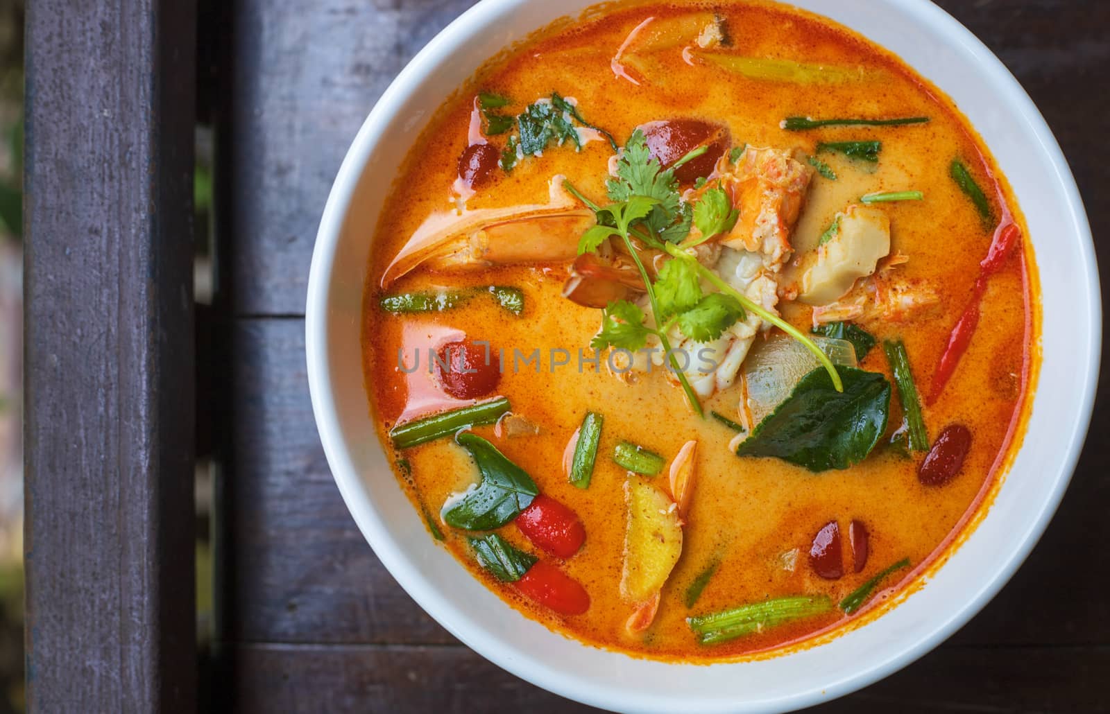 top view Tom Yam kung Spicy Thai soup with shrimp in white bowl on wood table. With copy space for text or design.