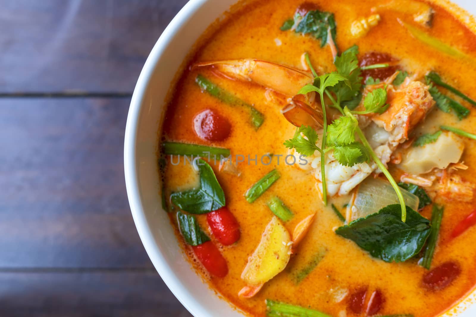 Top view Tom Yam kung Spicy Thai soup with shrimp in white bowl on wood table. With copy space for text or design.