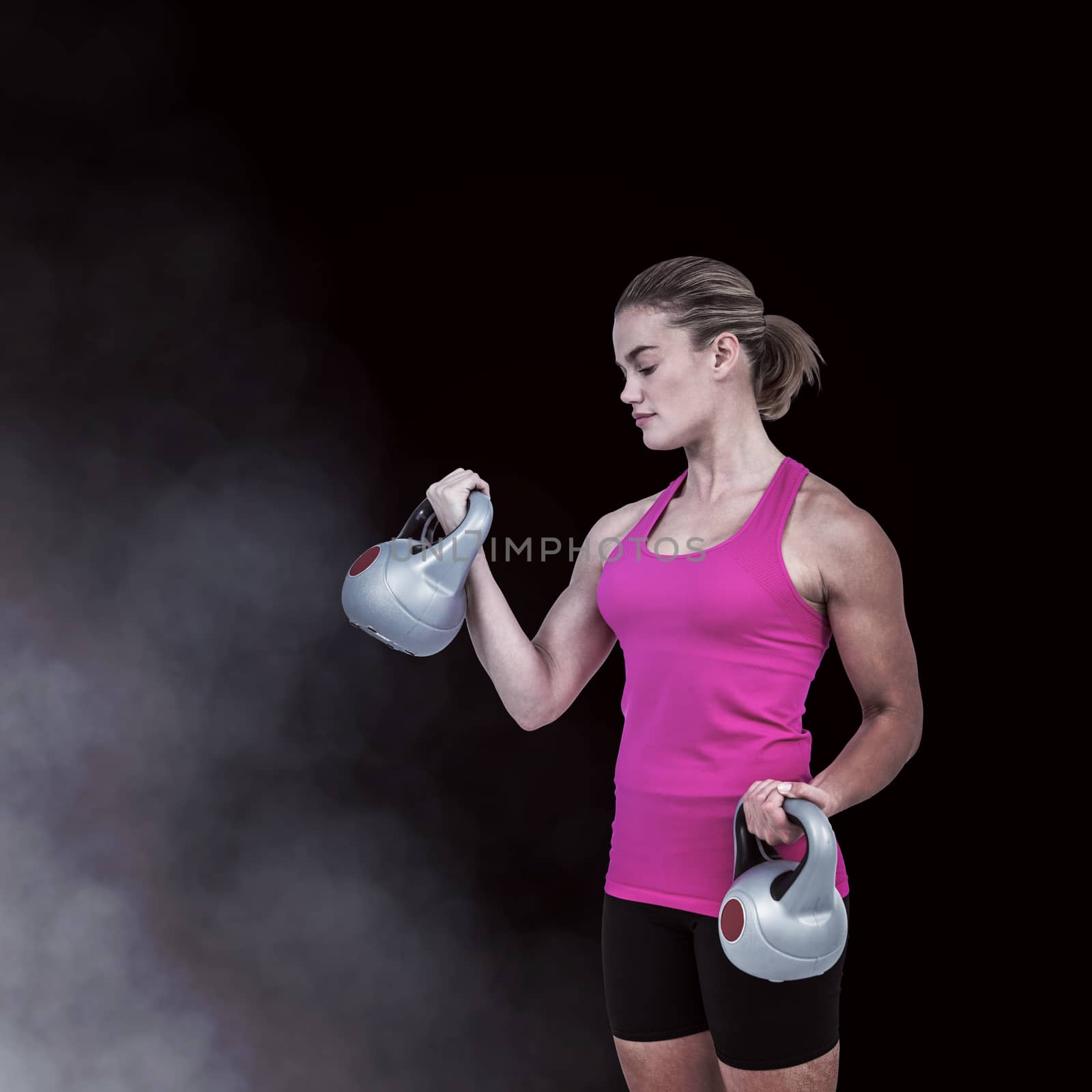 Muscular woman exercising with kettlebells against smoke on black background