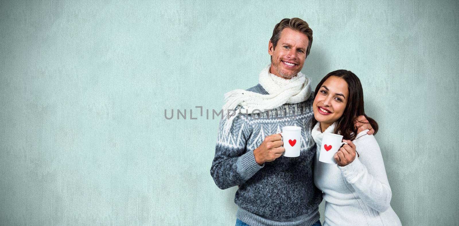 Festive couple smiling and holding mugs against blue background