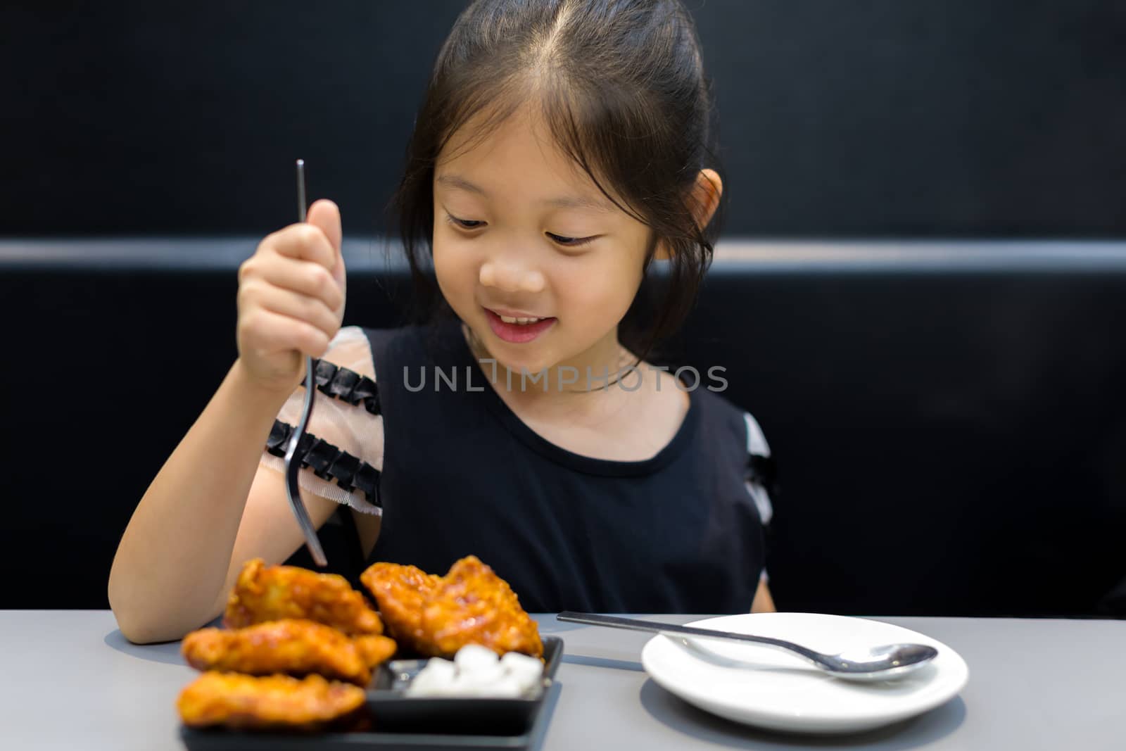 Hungry Asian child eating fried chicken at restaurant.