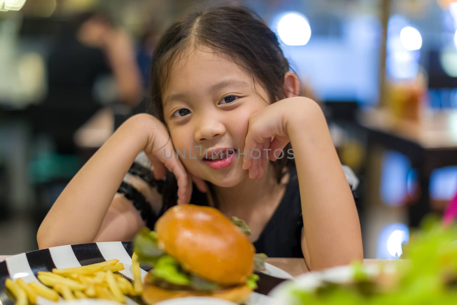 Hungry Asian child eating hamburger at restaurant.
