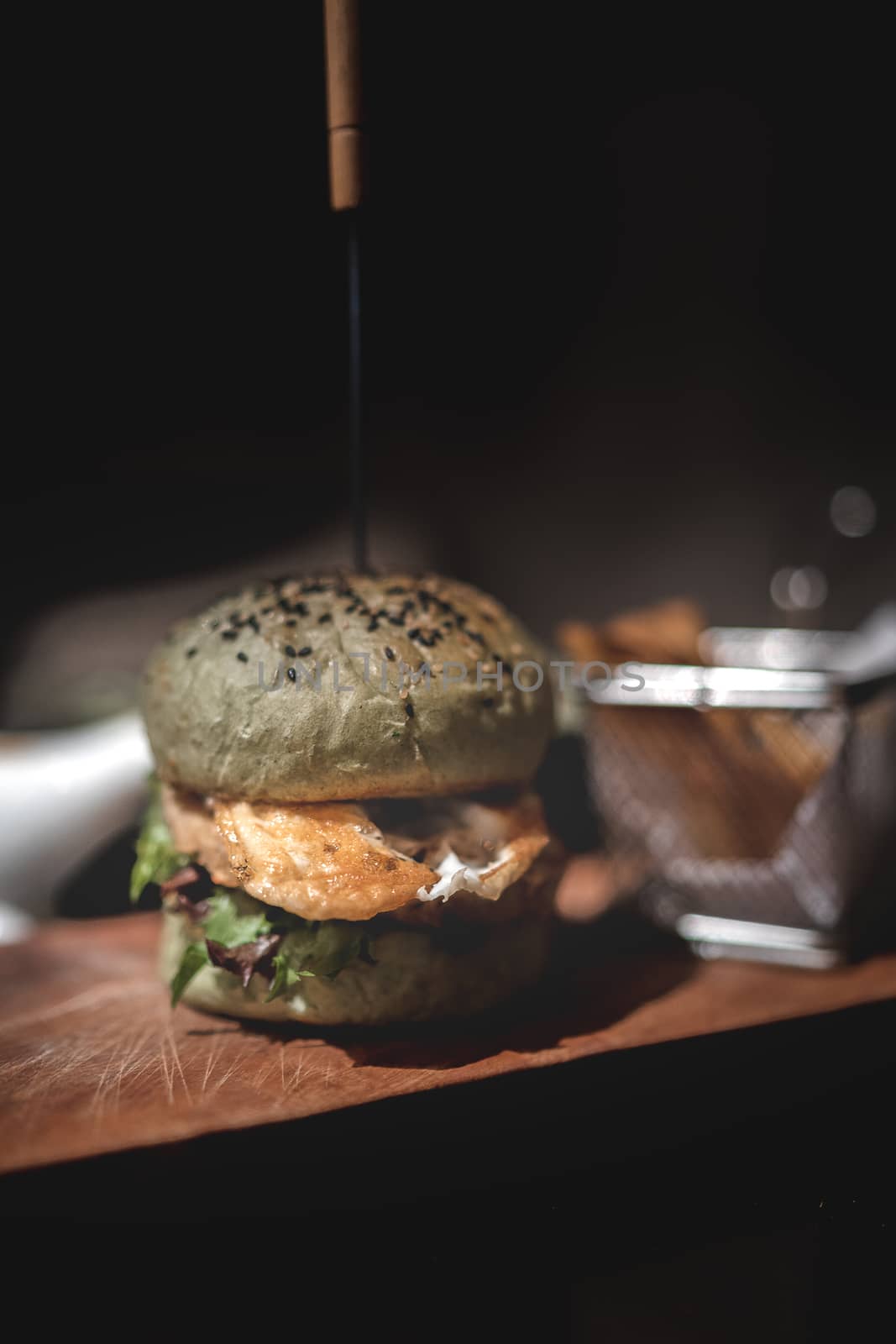 Burger and fries on wooden plate with black background.