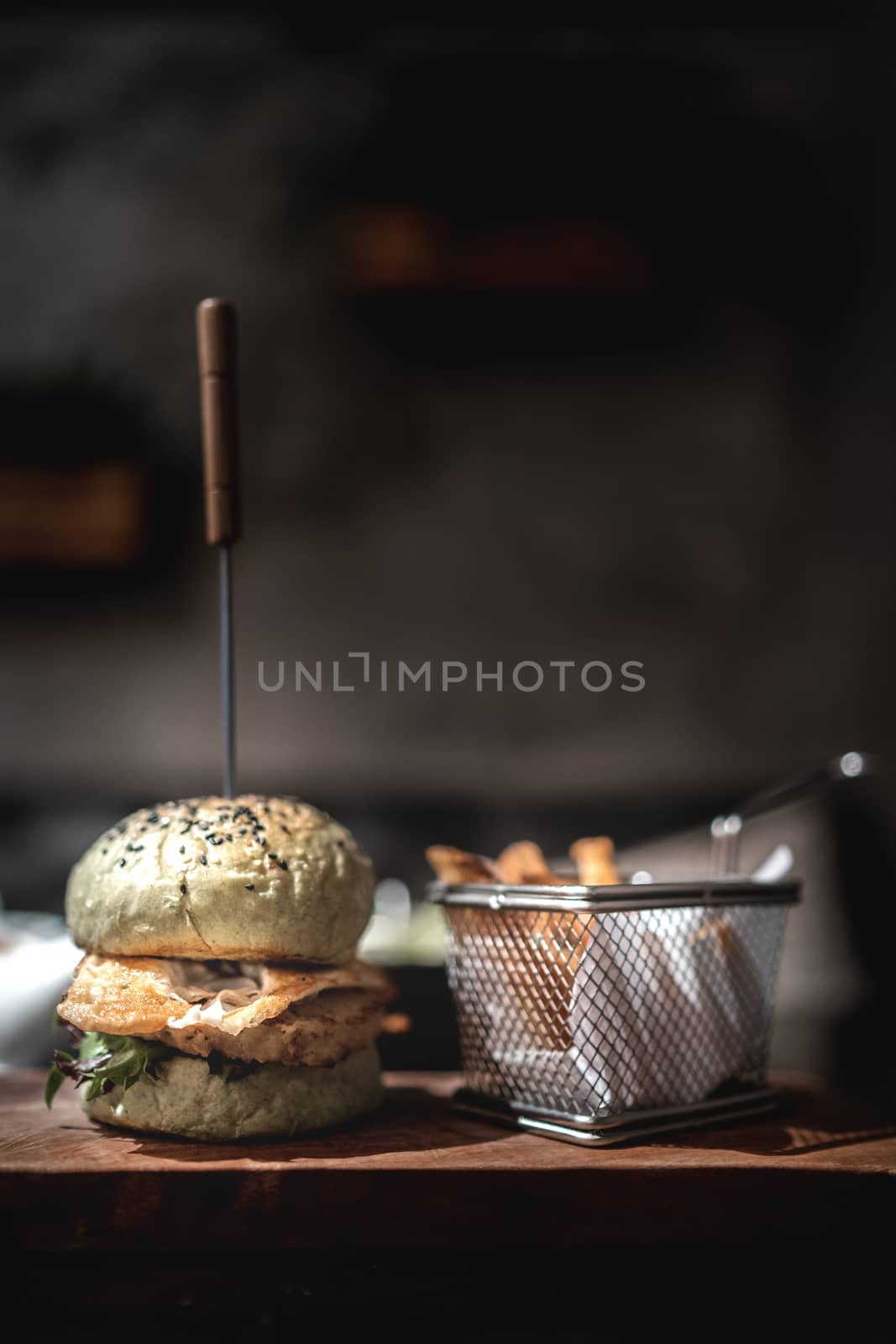 Burger and fries on wooden plate with black background.
