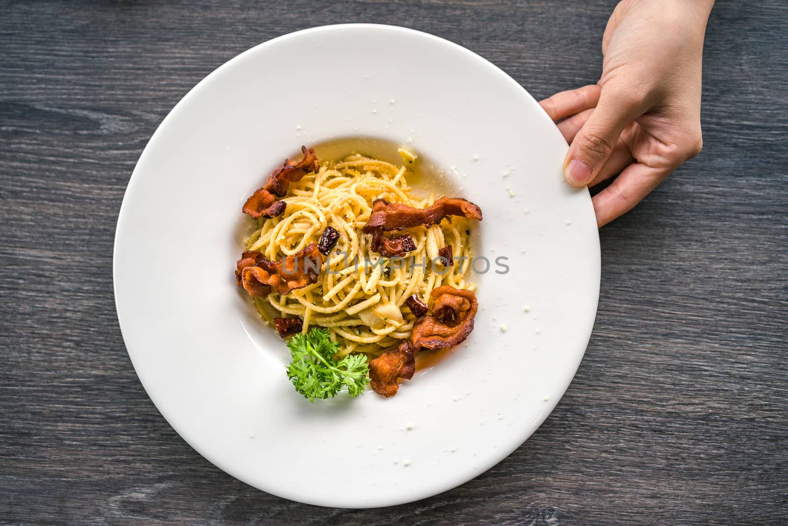 Top view of spaghetti with crispy bacon in white plate.