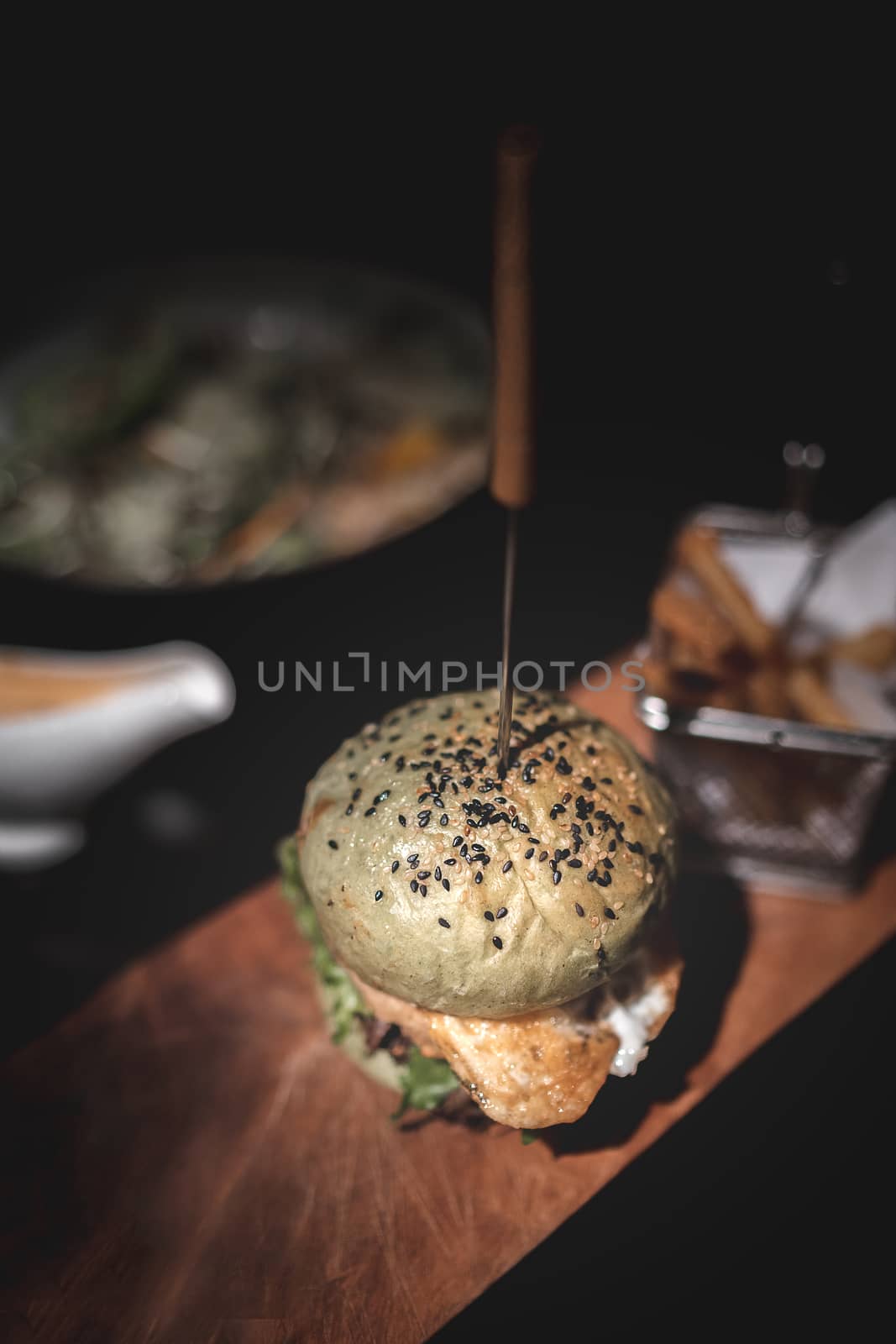 Burger and fries on wooden plate with black background.