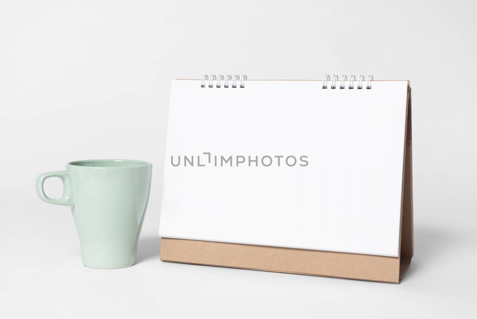 Blank paper spiral calendar for mockup template advertising and branding with cup on gray background.